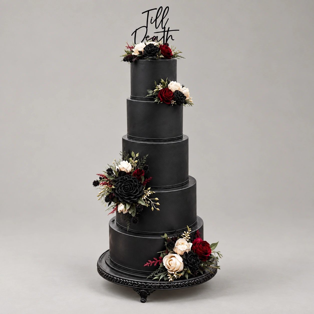 Five-tier black cake with clusters of red, black and ivory roses, green foliage and a black script topper