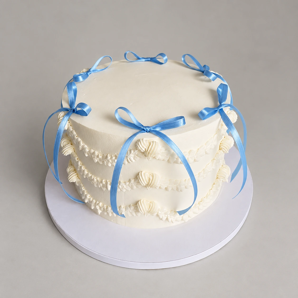 Round white cake with blue ribbon bows, piped swags and shell borders