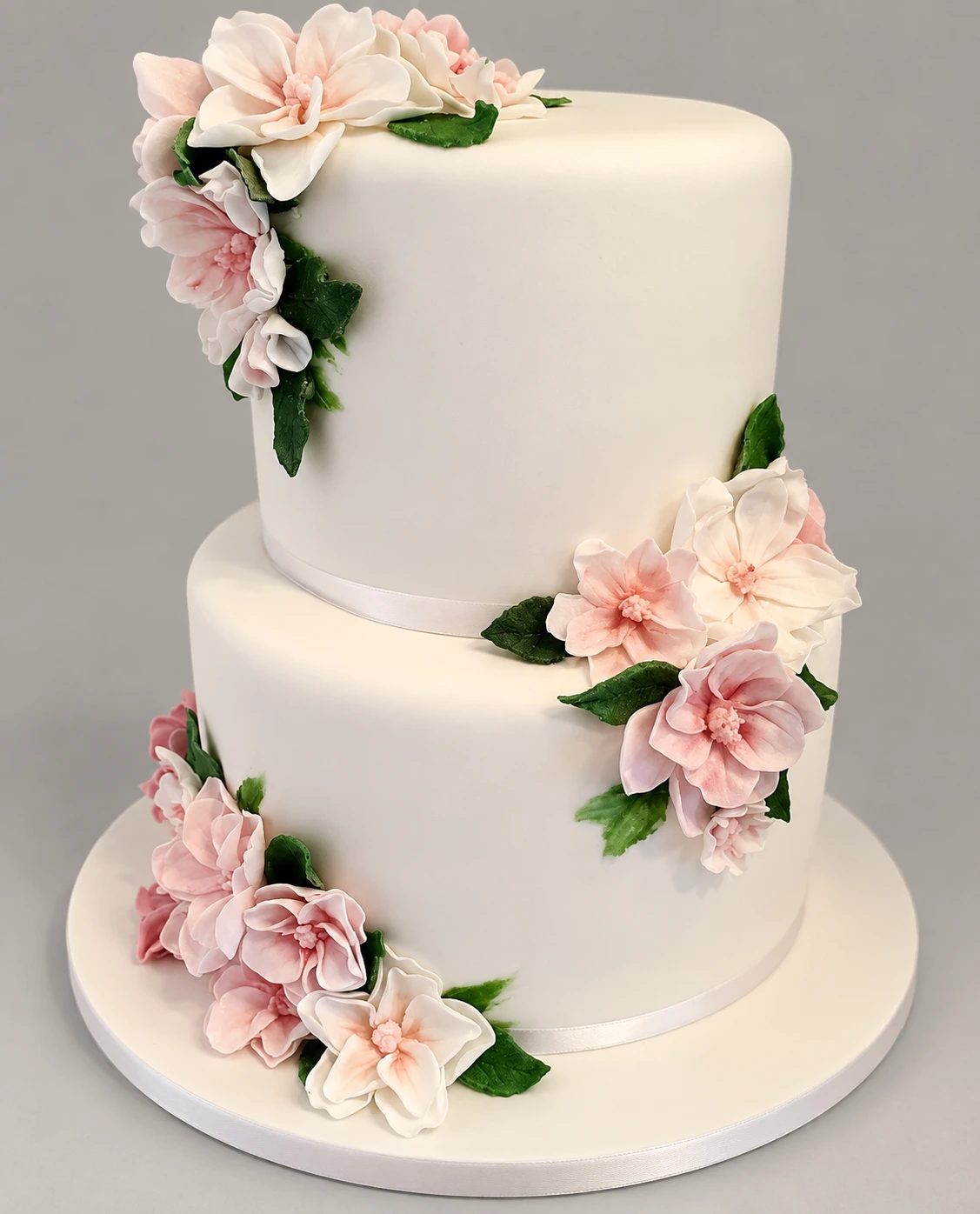 Two-tier white cake with pink fondant flowers and green leaves