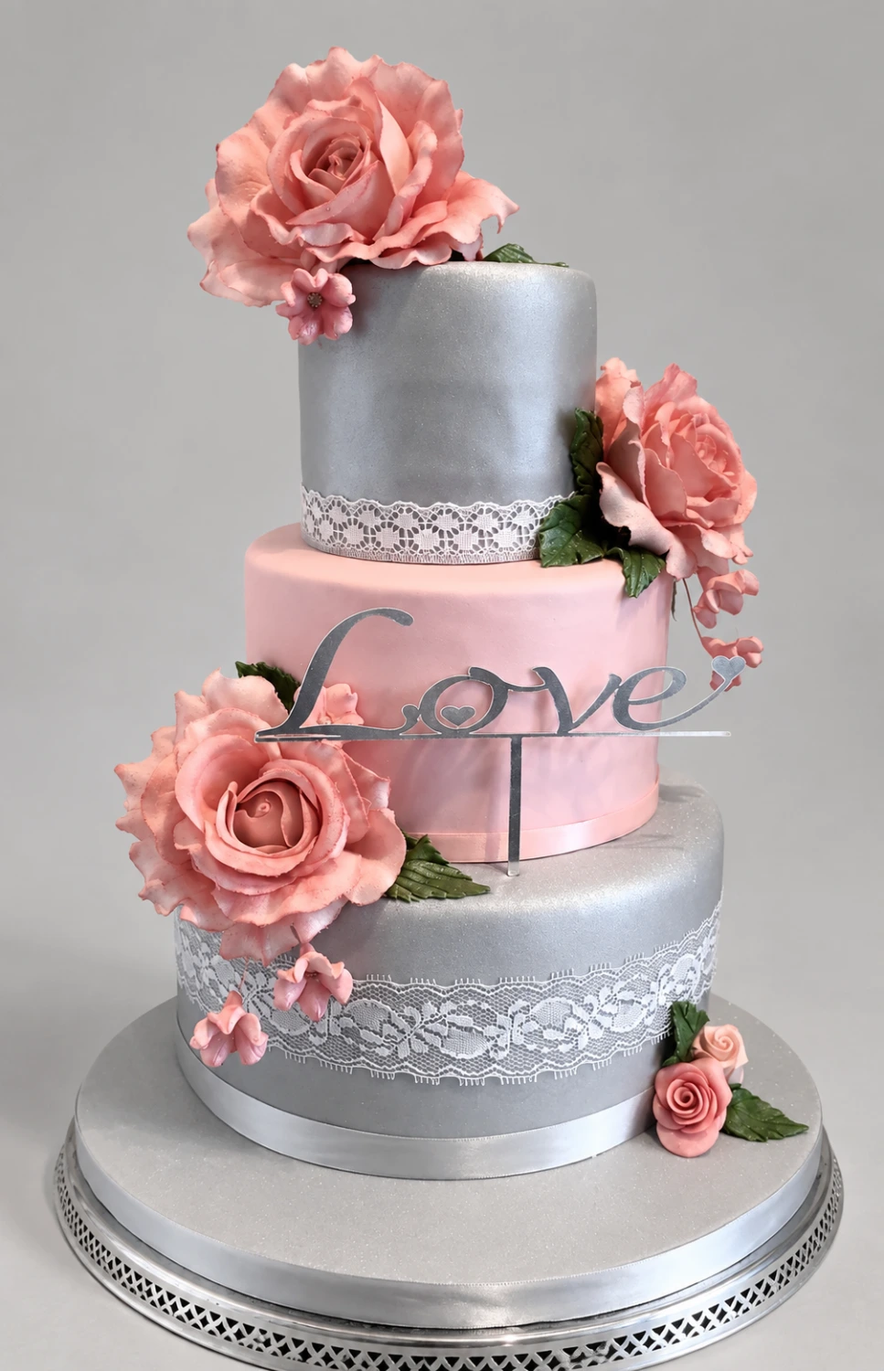 Three-tier pink and silver cake with lace bands, pink roses and a Love decoration