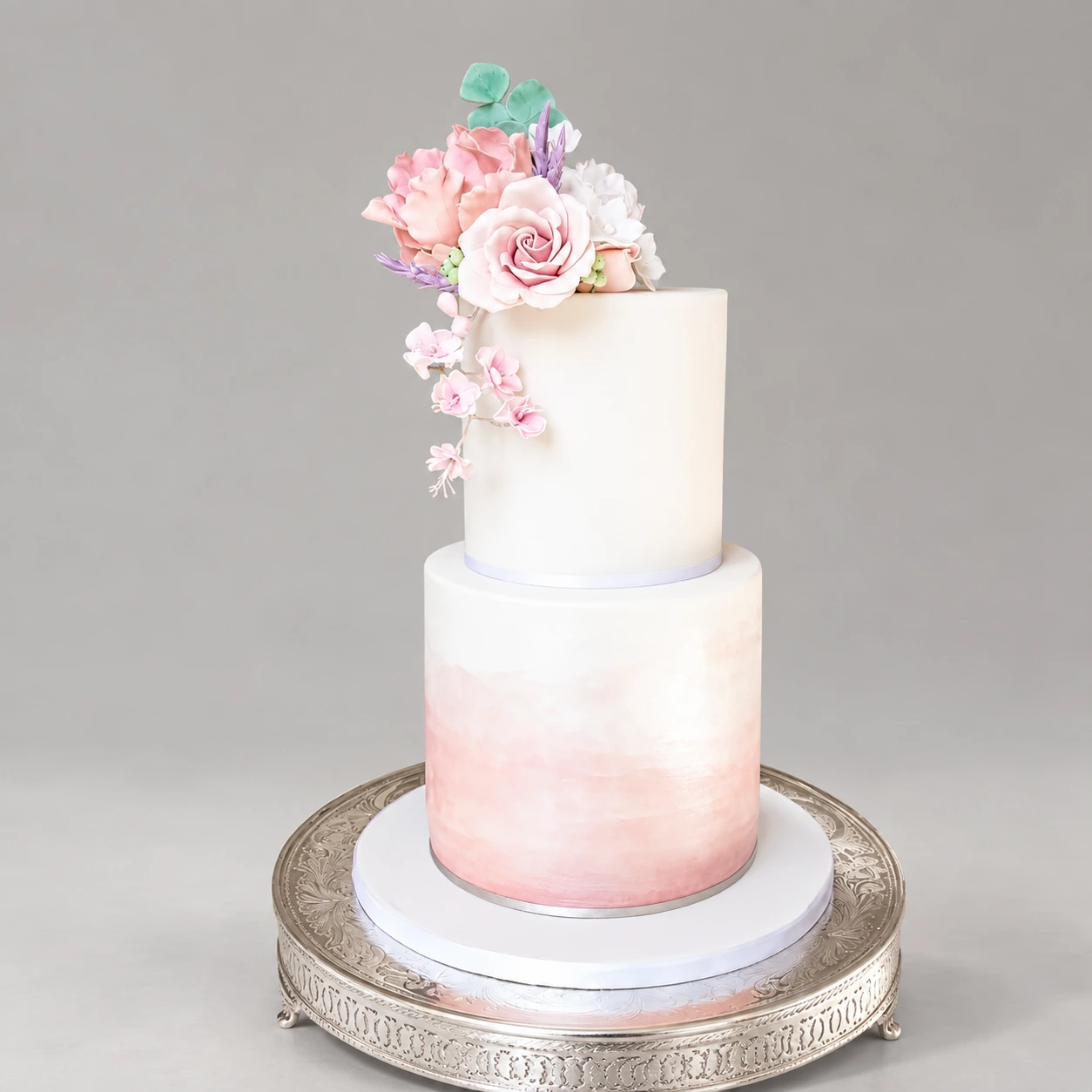 Two-tier white cake with a blush watercolour base and pastel pink and blue sugar flowers