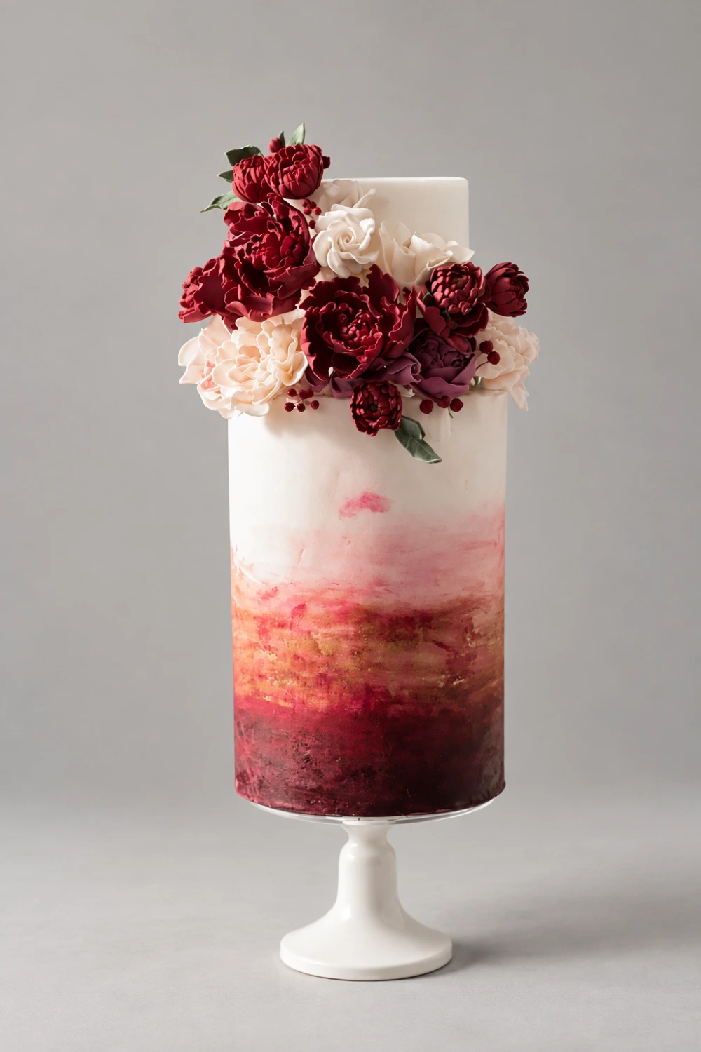 Tall single-tier cake with burgundy watercolour shading and a red and ivory sugar flower crown