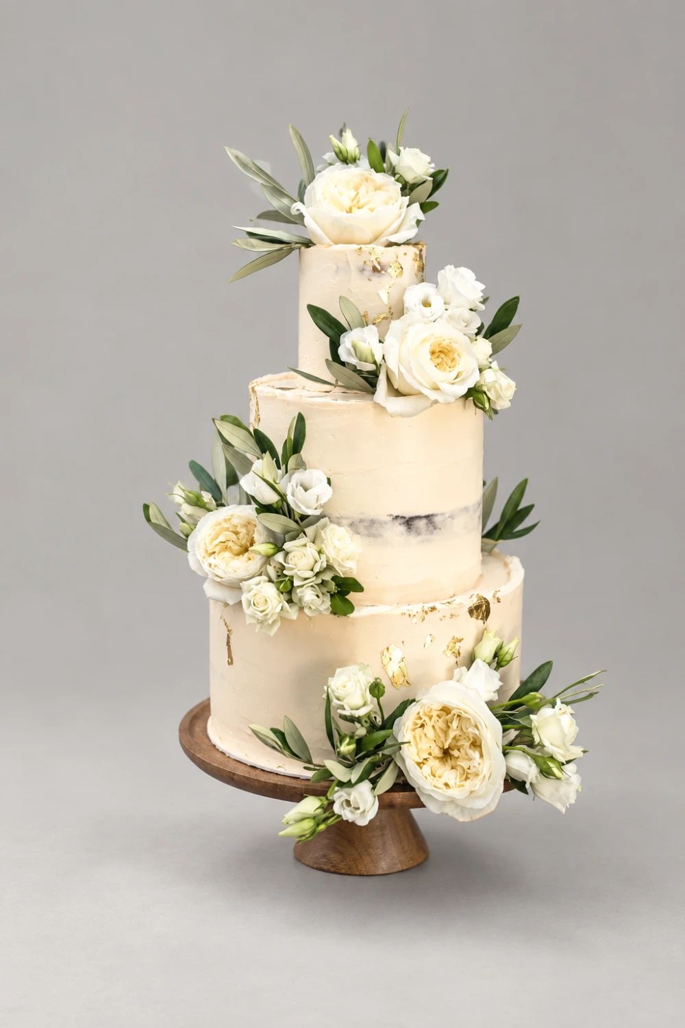 Three-tier semi-naked cake with cream roses, peonies, foliage and gold leaf