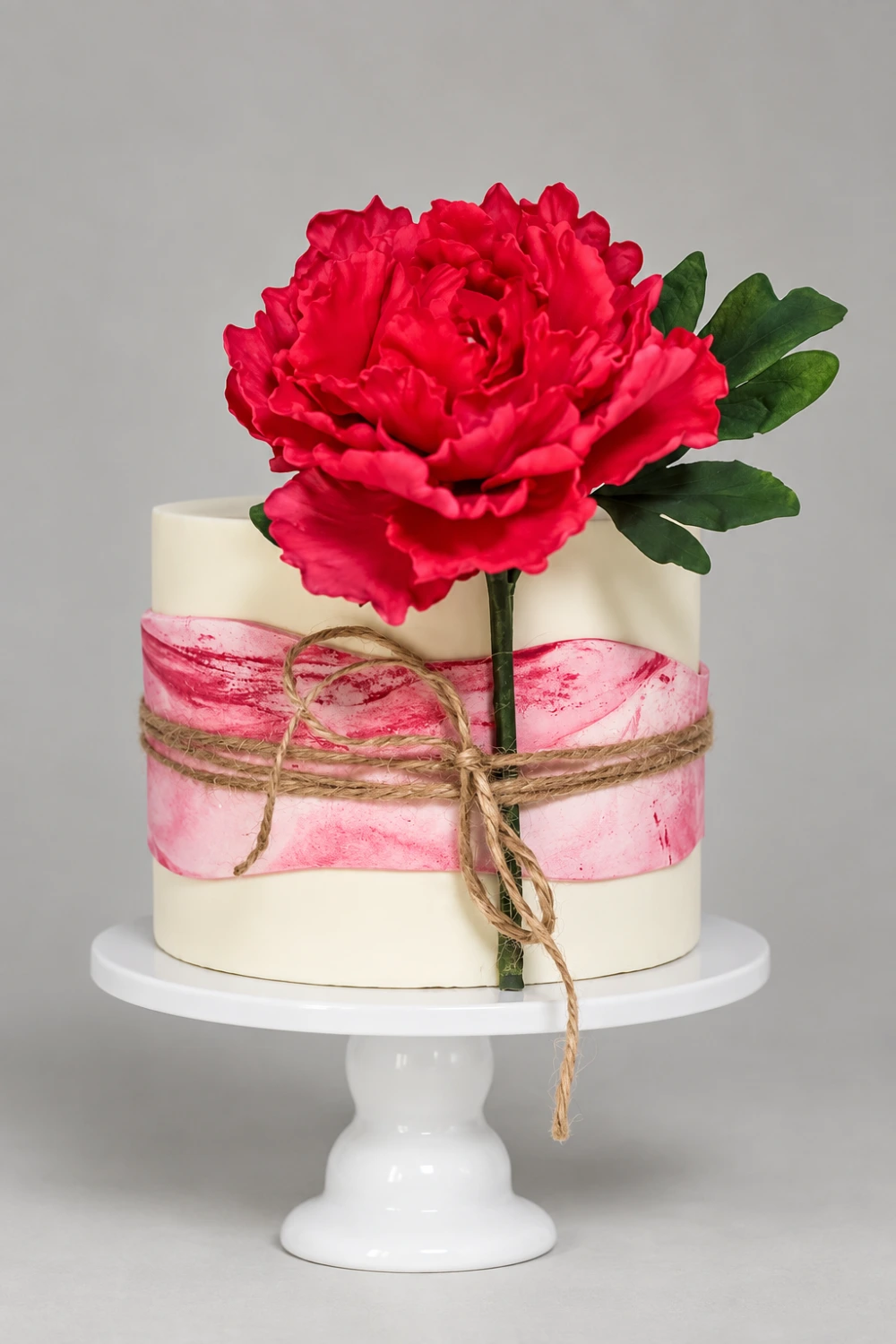 Single-tier ivory cake with a crimson sugar peony, pink wrap and twine detail