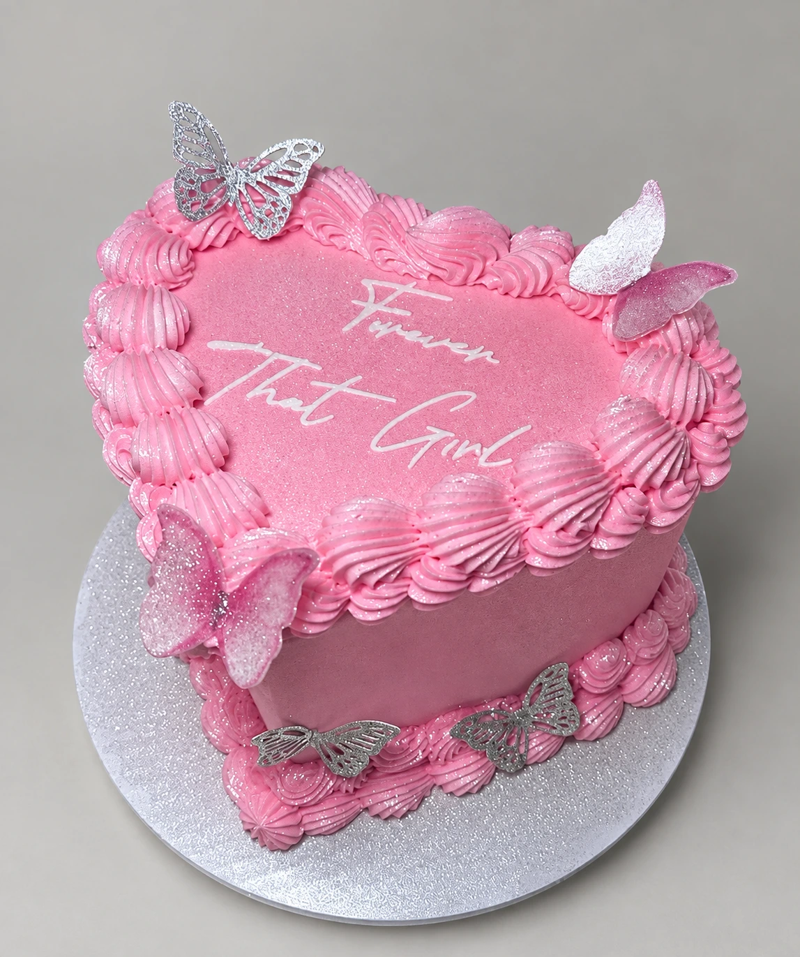 Pink heart-shaped cake with piped shell borders, butterfly decorations and a written message