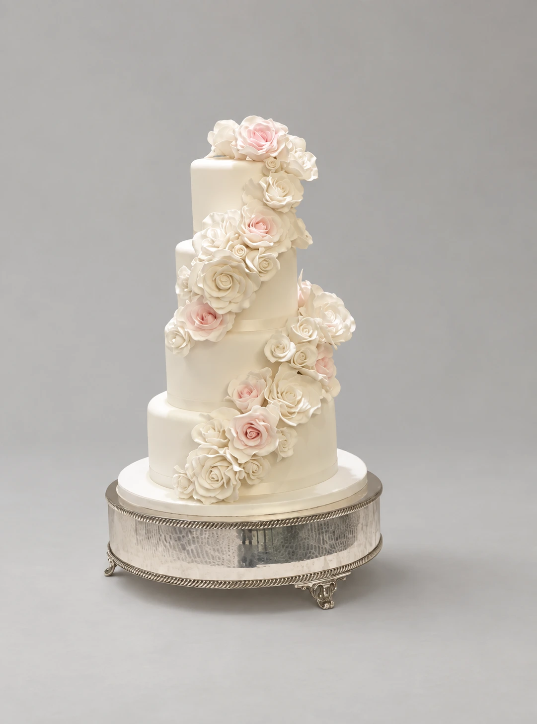 Four-tier white wedding cake with a winding cascade of ivory and blush sugar roses