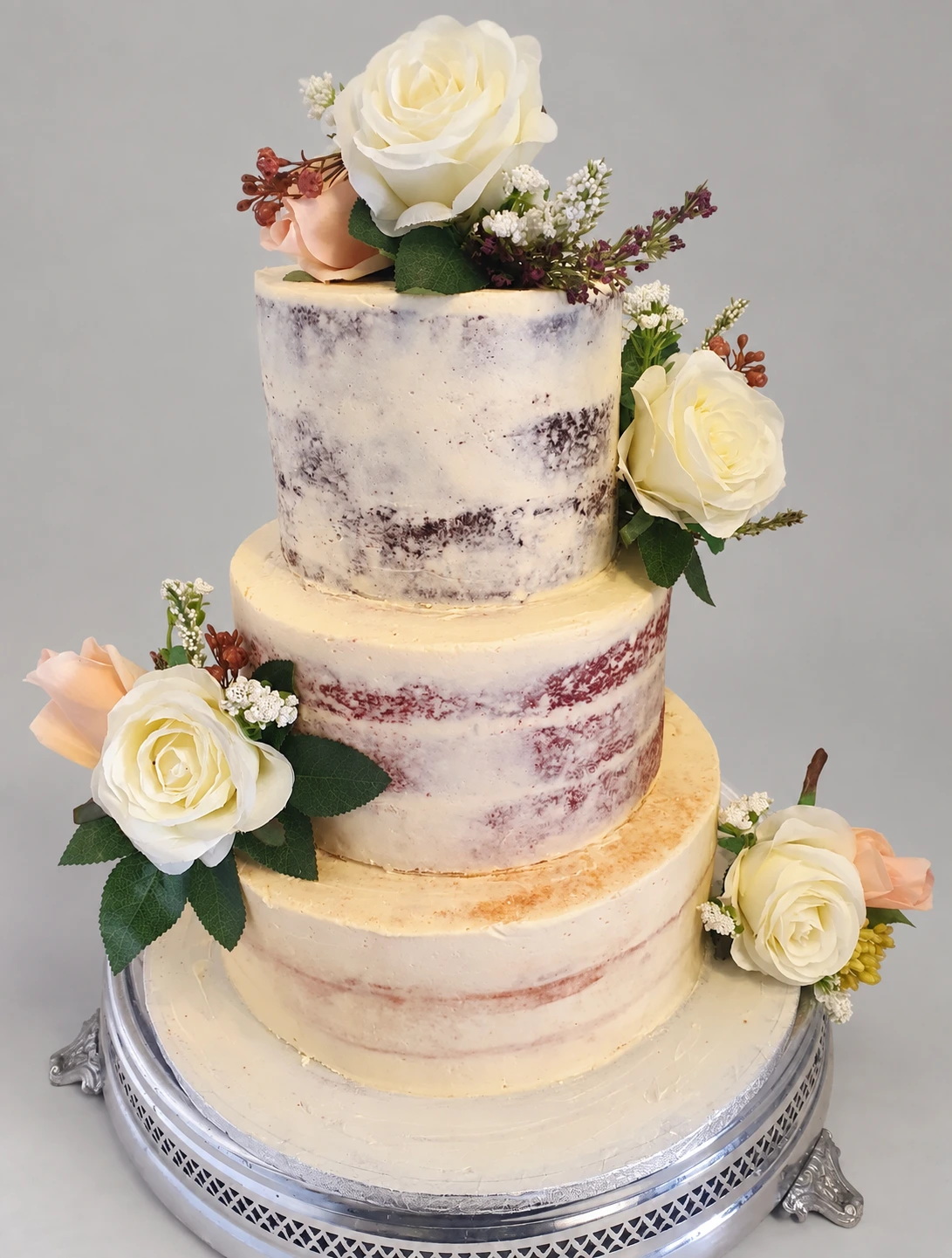 Three-tier semi-naked cake decorated with fresh cream and blush roses