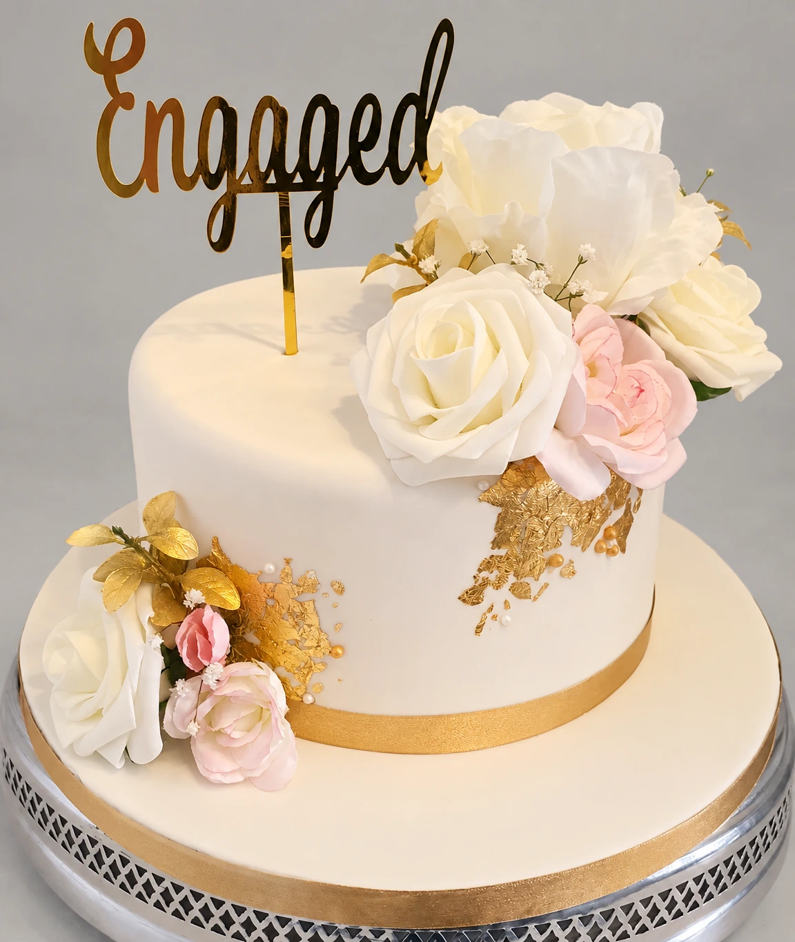 Single-tier ivory cake with pale roses, gold accents and an Engaged topper