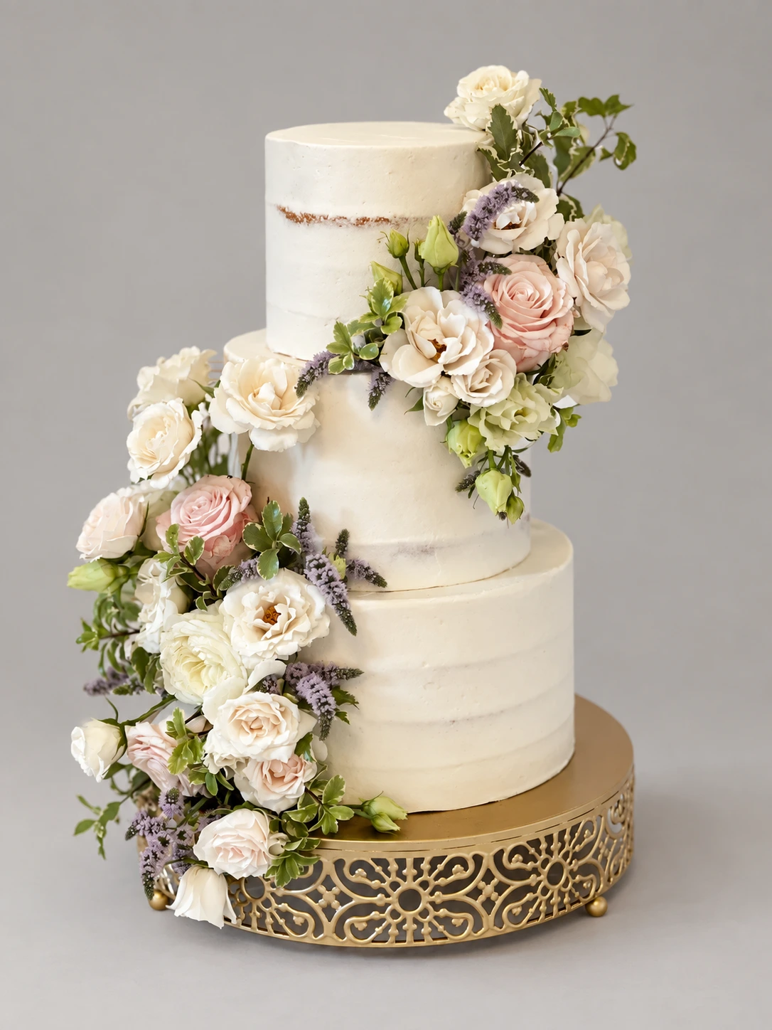 Three-tier semi-naked cake with cream and blush roses, lavender and a green floral cascade