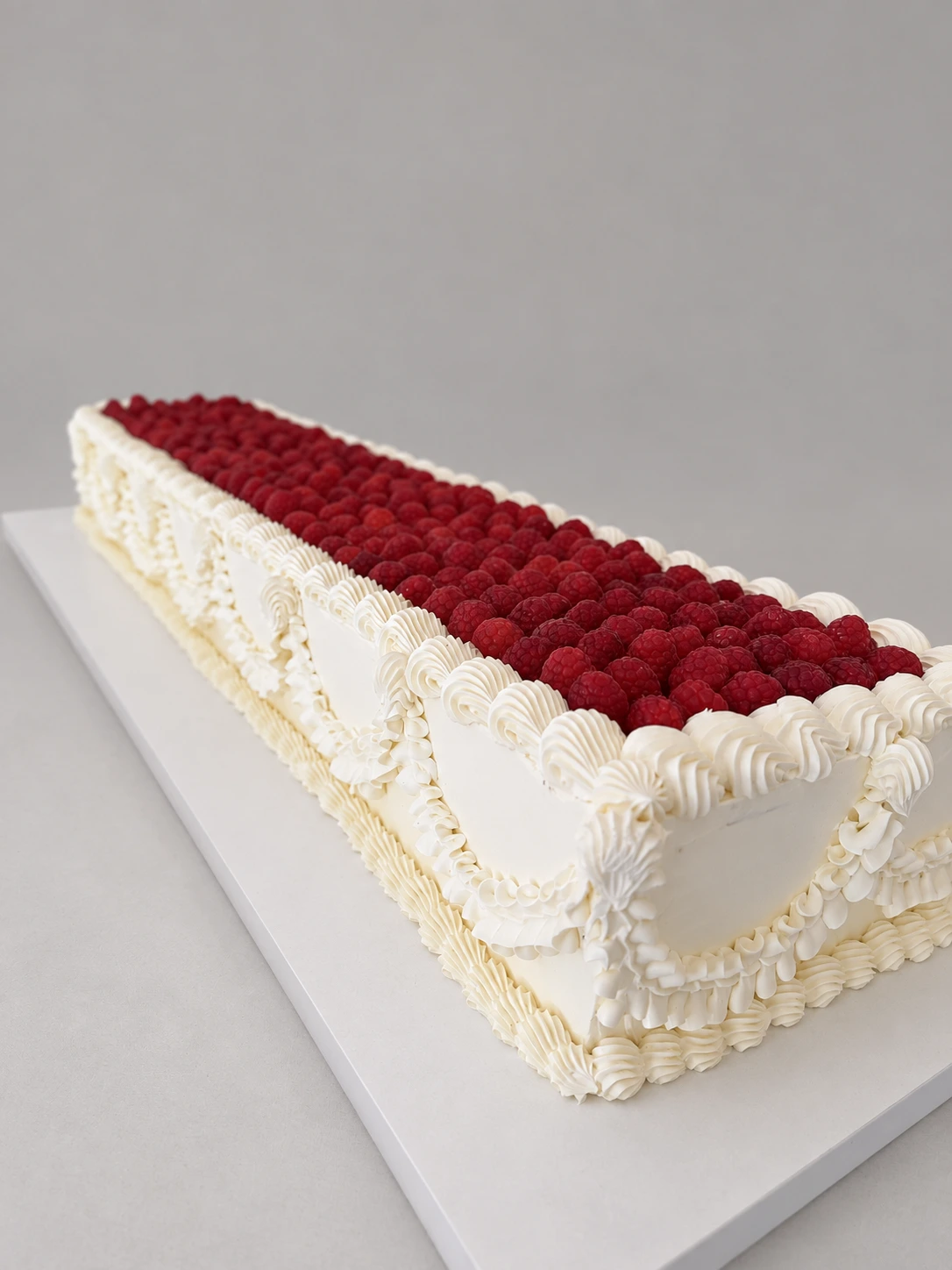 Long rectangular white cake topped with raspberries and decorated with piped swags and shell borders