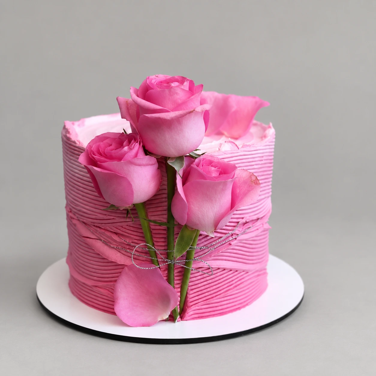 Round pink cake with ridged icing, pink roses and green stems