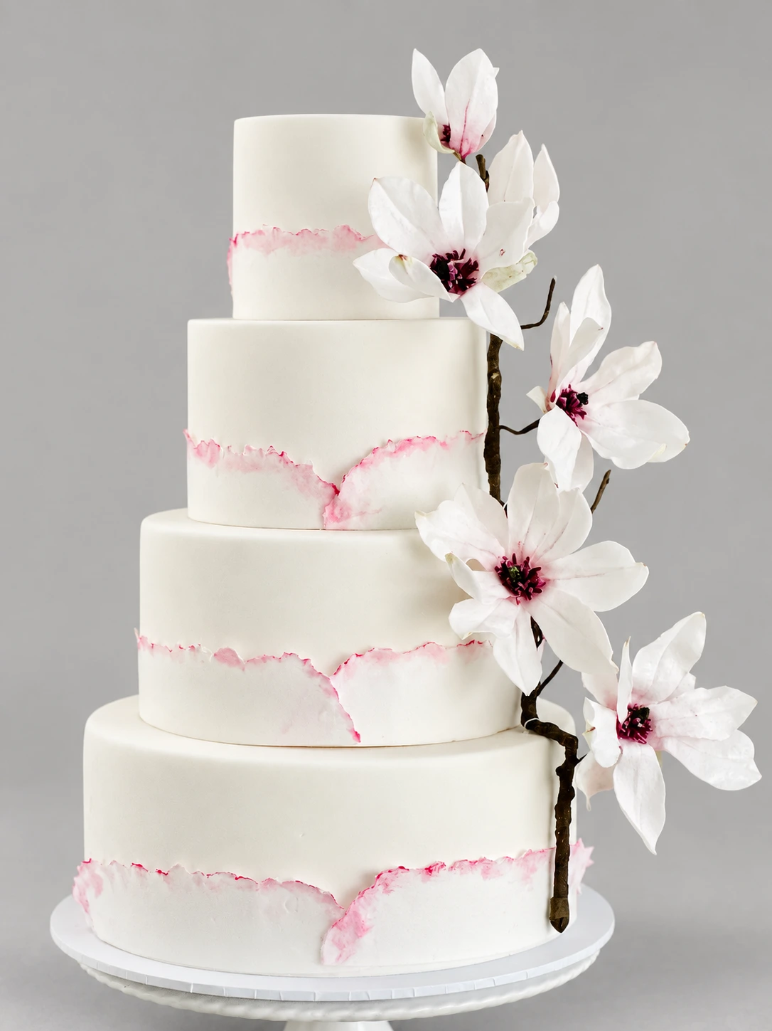 Four-tier ivory cake with torn blush marble edges and a white sugar magnolia branch
