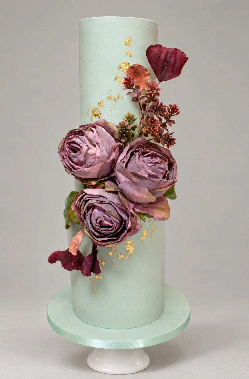Two-tier pale mint cake with mauve sugar roses, burgundy flowers and gold leaf
