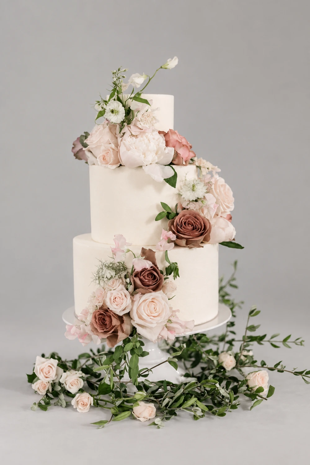 Three-tier ivory cake with mocha and blush fresh roses and loose green foliage