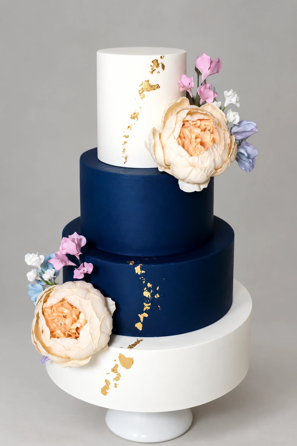 Four-tier navy and ivory cake with large peach sugar peonies, small pastel flowers and gold leaf