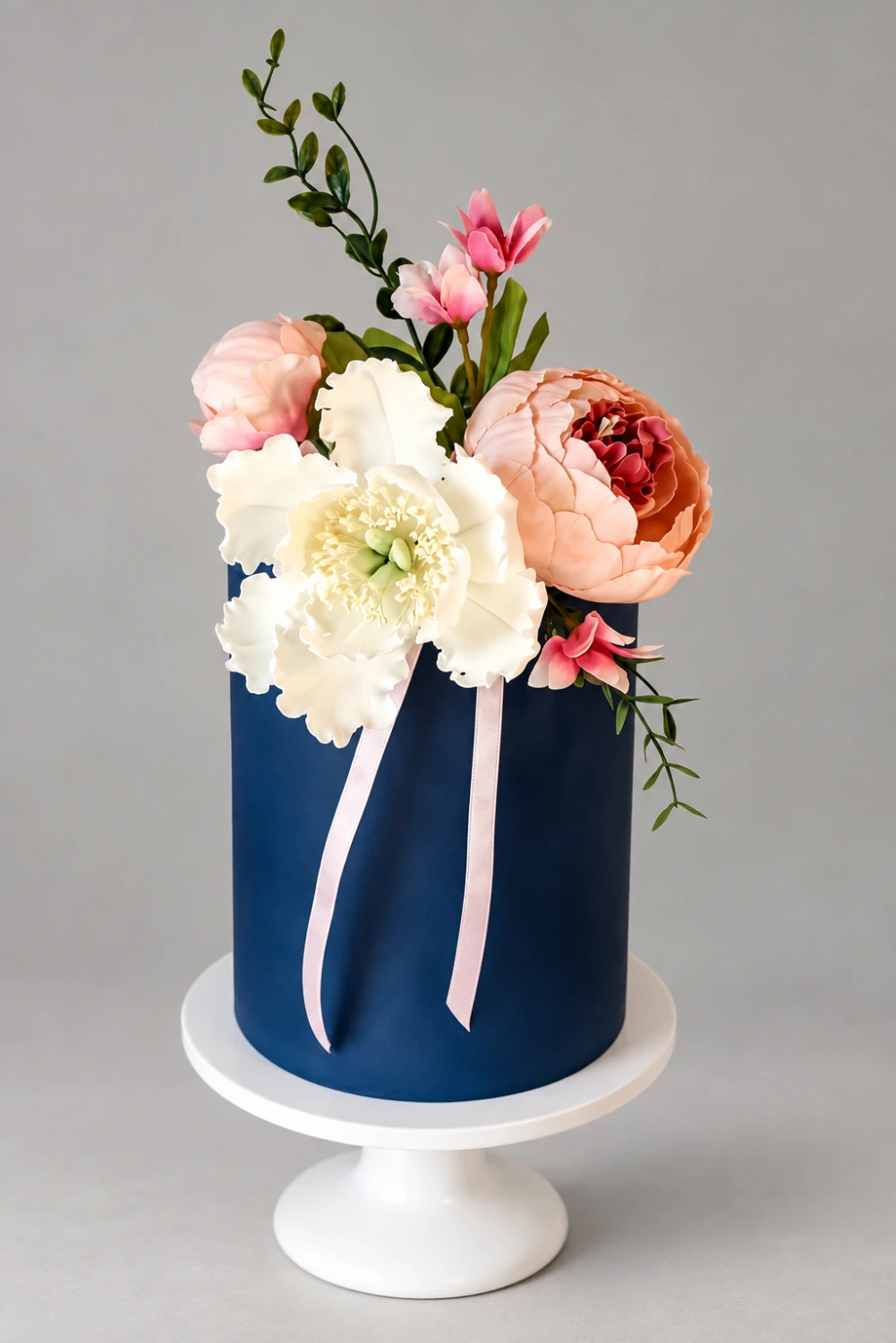 Tall single-tier navy cake with white and peach sugar peonies, small pink flowers and blush ribbon