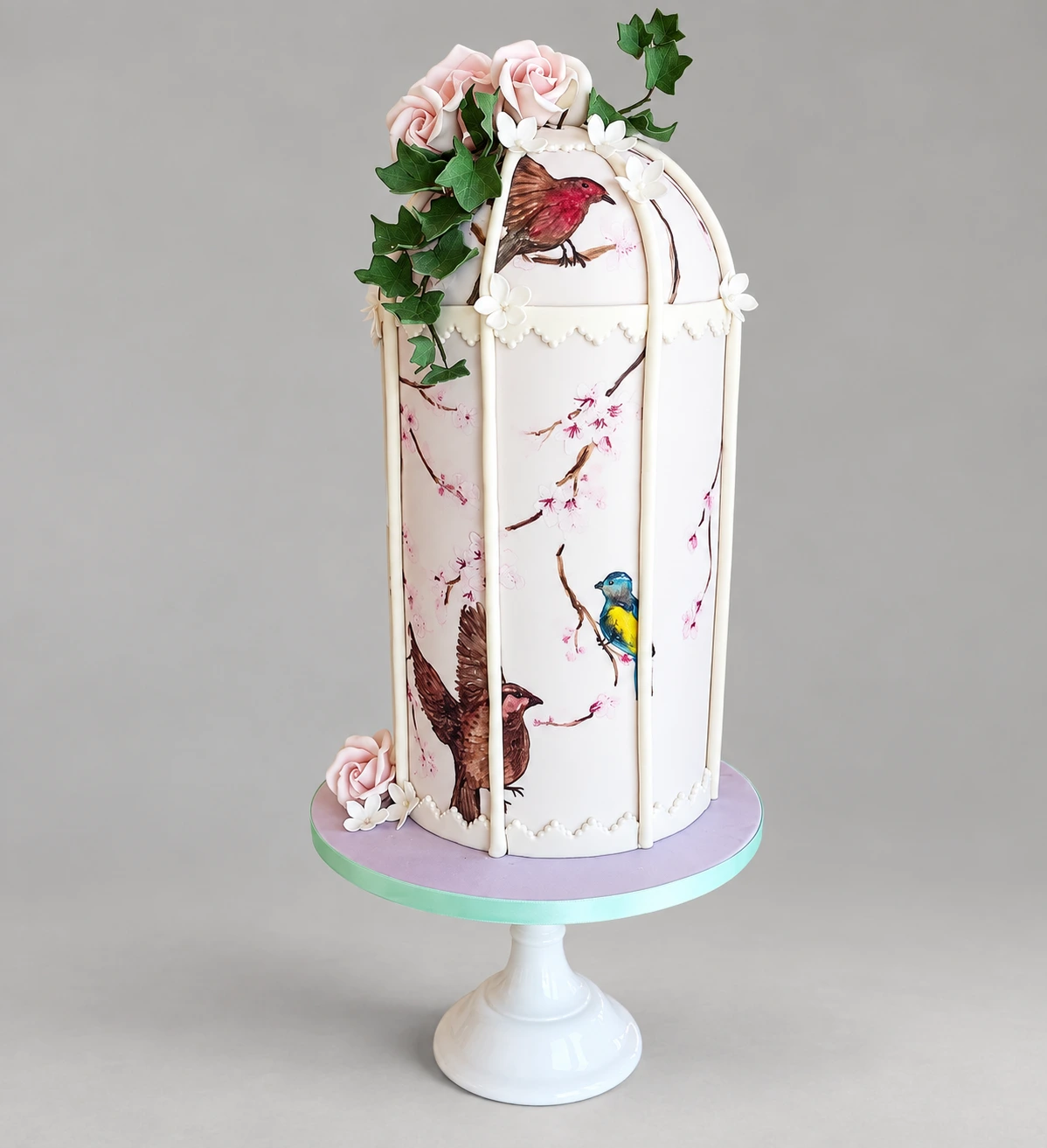 Tall single-tier birdcage-shaped cake with painted birds, delicate branches and pale sugar roses