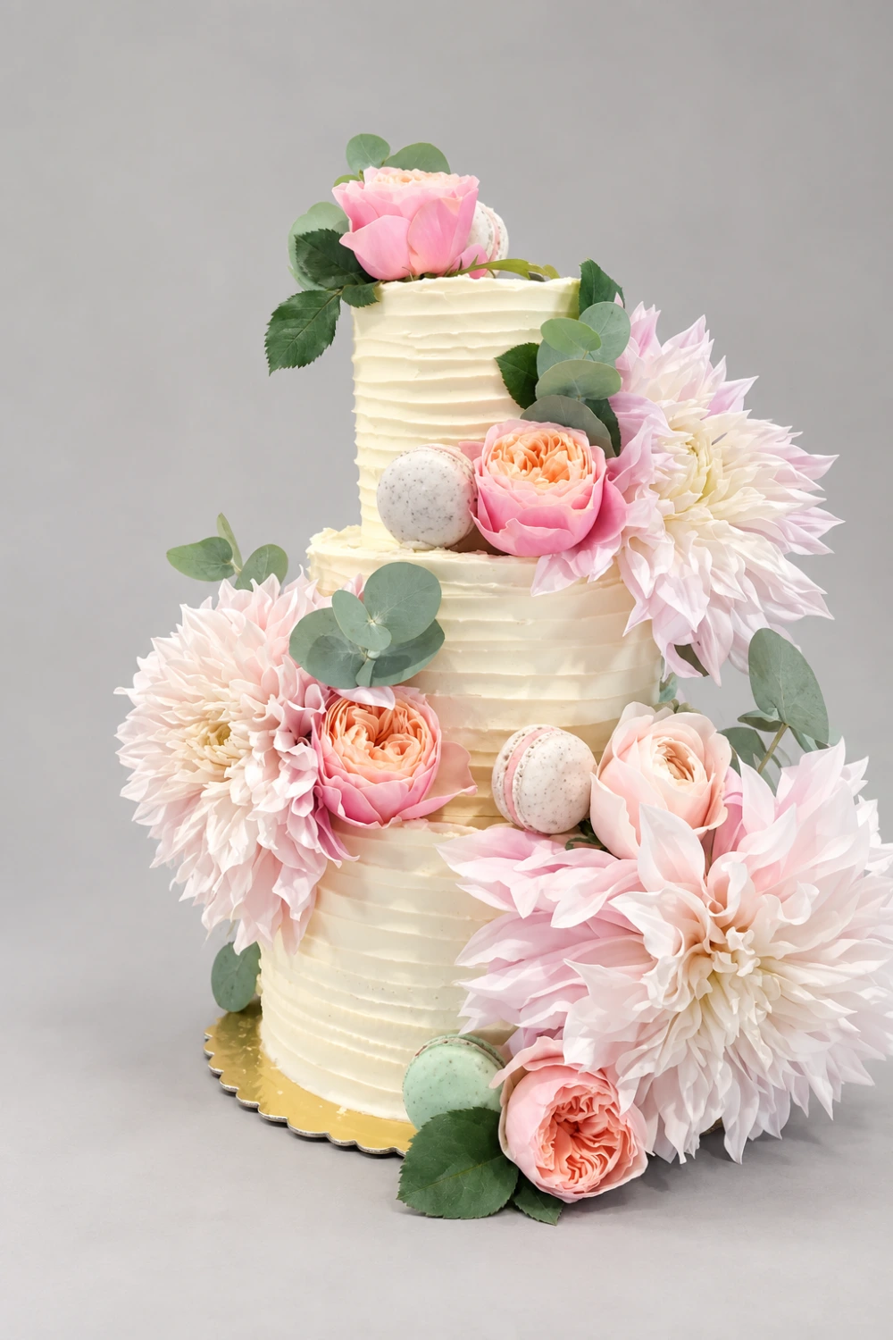 Three-tier rippled ivory cake with large pale pink dahlias, pink roses, foliage and macarons