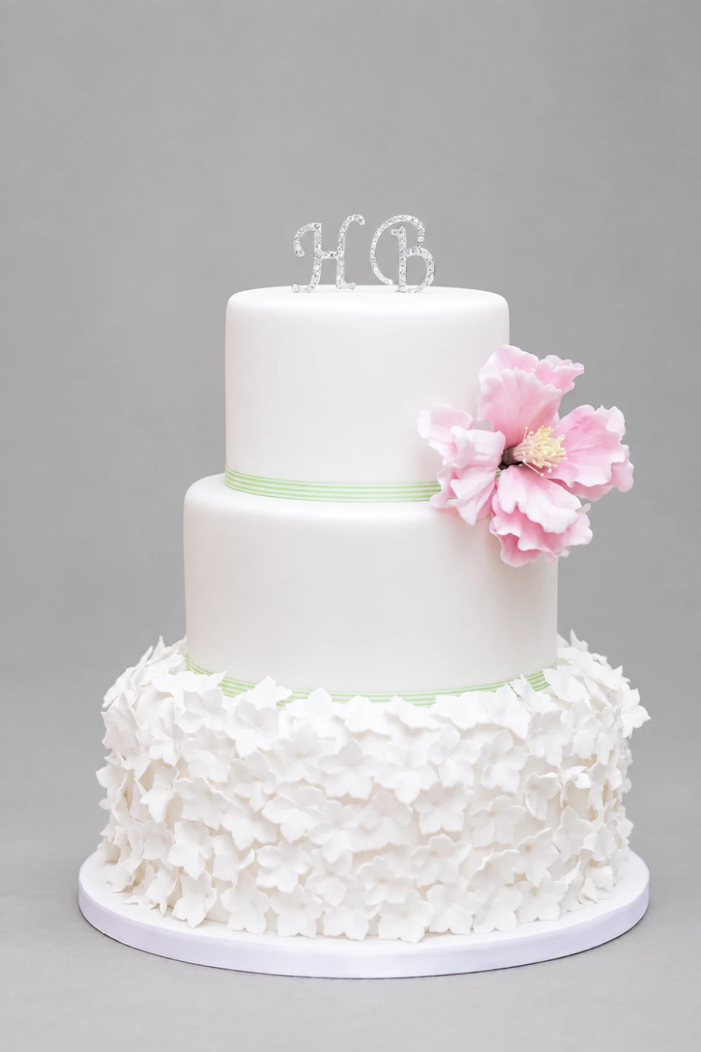 Three-tier white cake with a hydrangea-covered base, pink sugar peony and initial topper