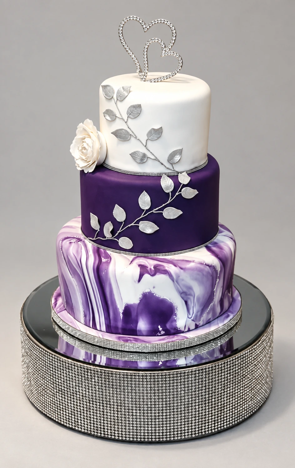Three-tier purple and white cake with a marbled base, silver leaves and interlocking heart topper