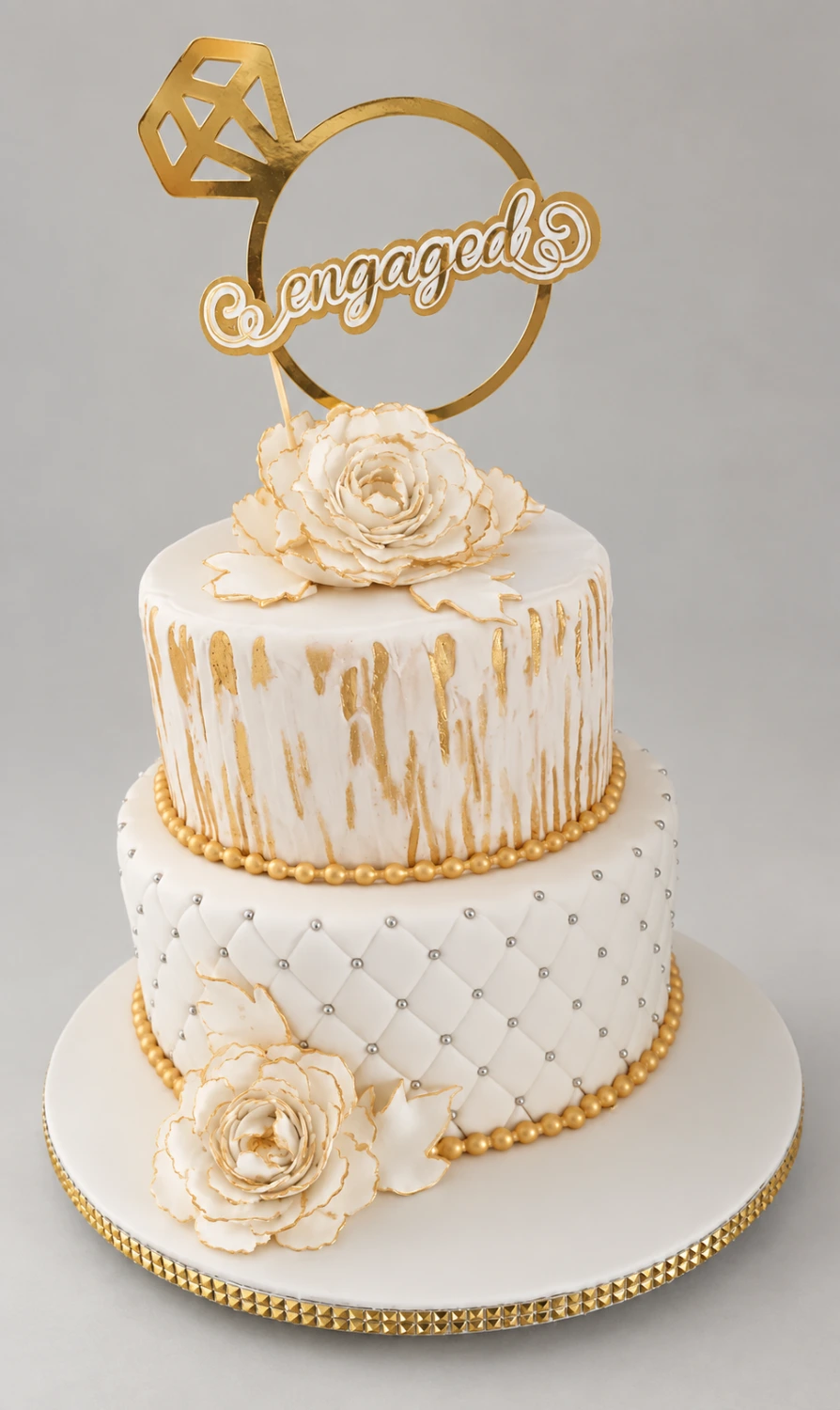 Two-tier white cake with quilted icing, gold drips, roses and a ring-shaped engagement topper