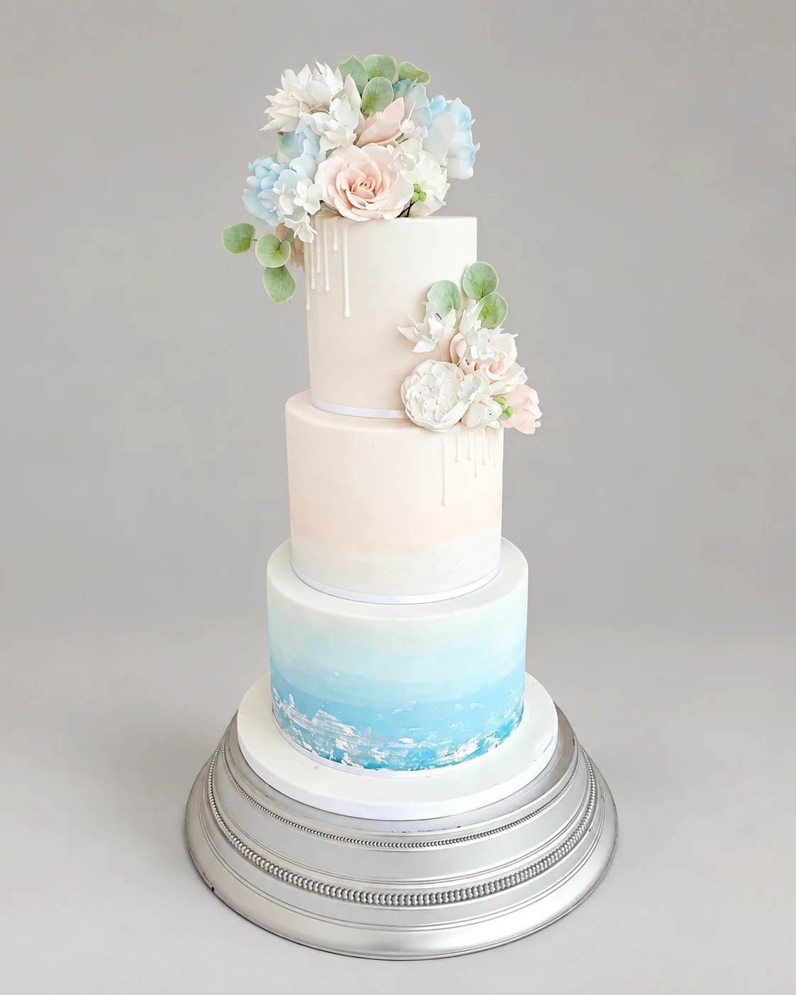 Three-tier ivory cake with a sky blue watercolour base and pale sugar flowers