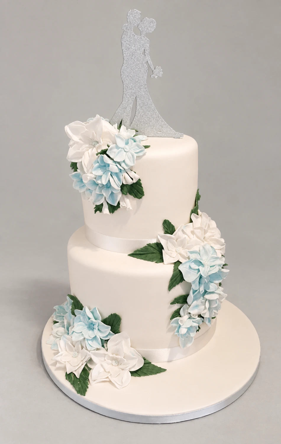 Two-tier pale pink cake with cascading blue and white fondant flowers and a couple topper
