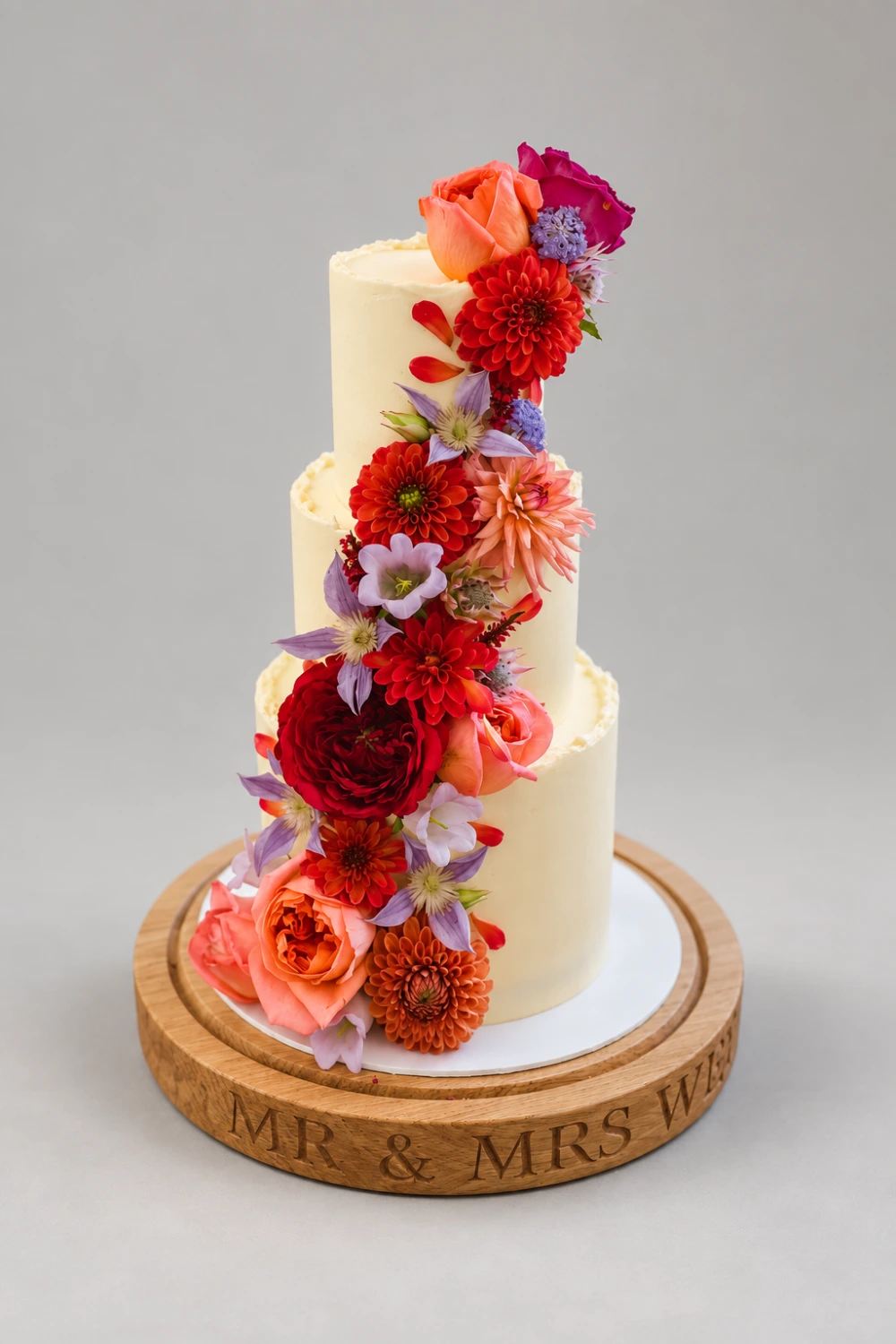 Three-tier white cake with a cascade of orange roses, red dahlias and small purple flowers