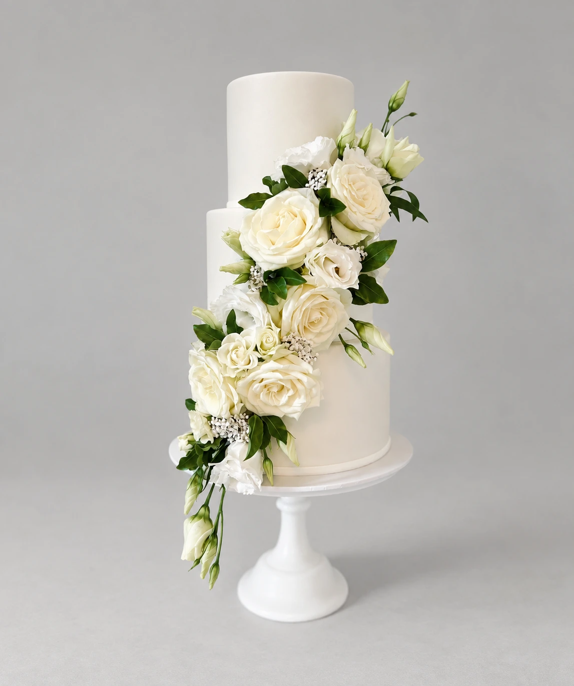 Three-tier white wedding cake with a cascade of white roses, lisianthus and green leaves