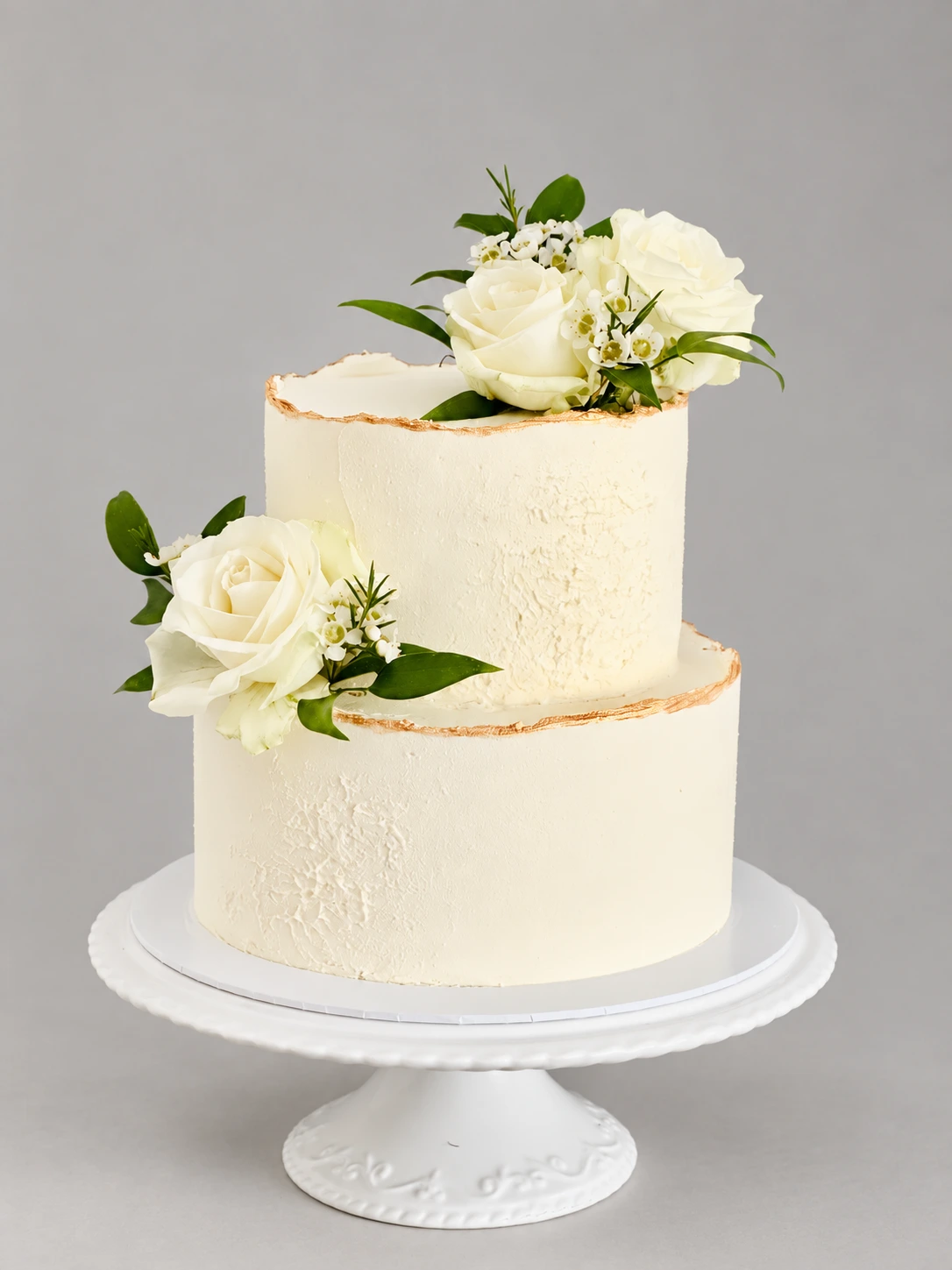 Two-tier semi-naked white wedding cake with ivory roses and green leaves
