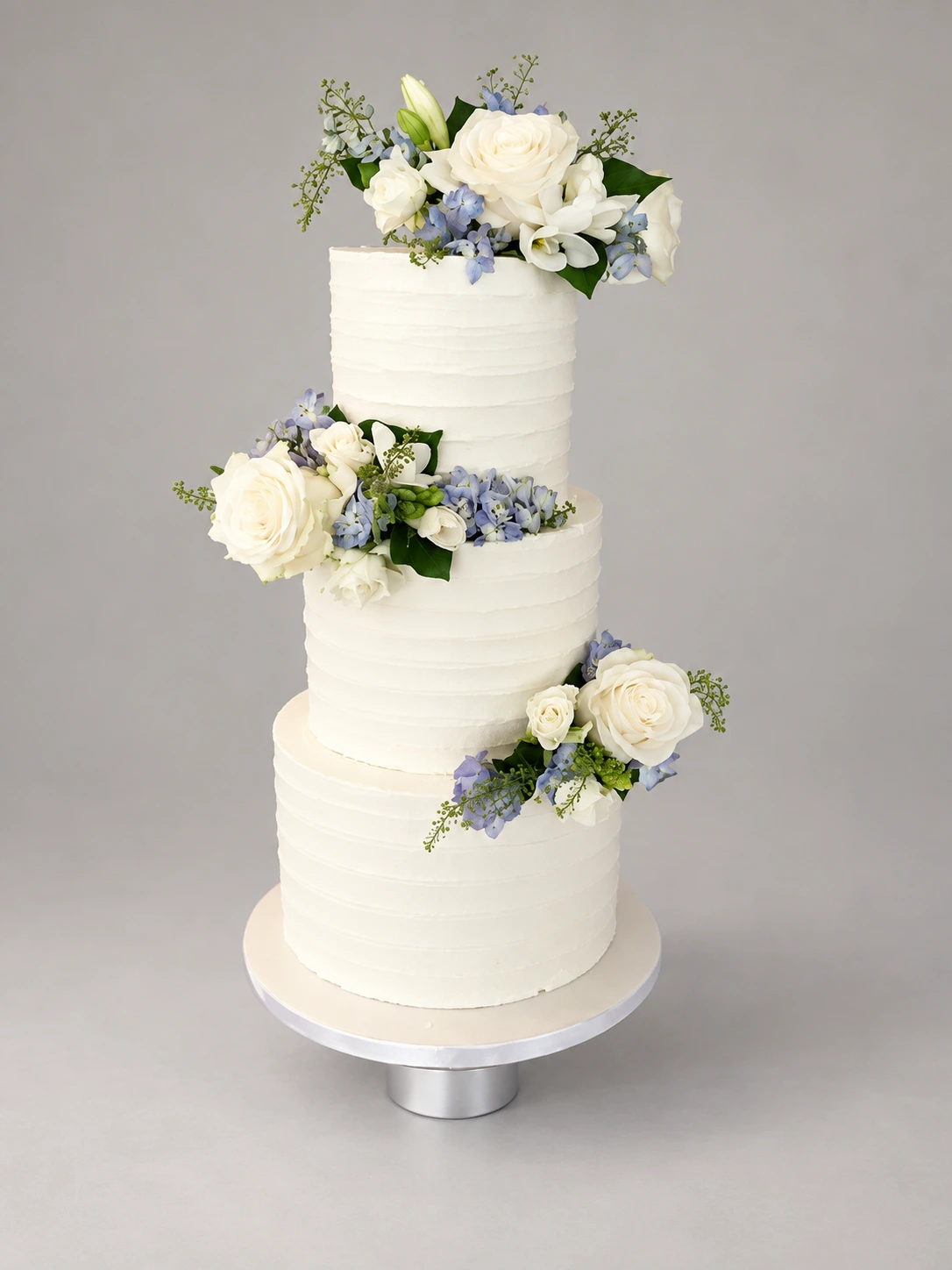 Three-tier ridged white cake with cream roses, pale blue flowers and green foliage