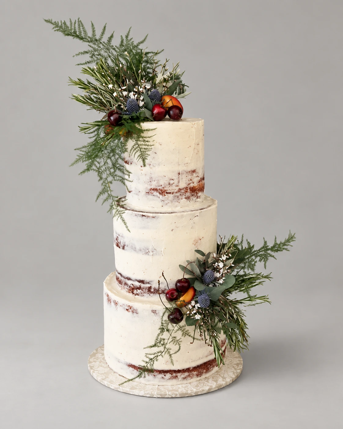Three-tier semi-naked cake with blue thistles, foliage and dark fruit