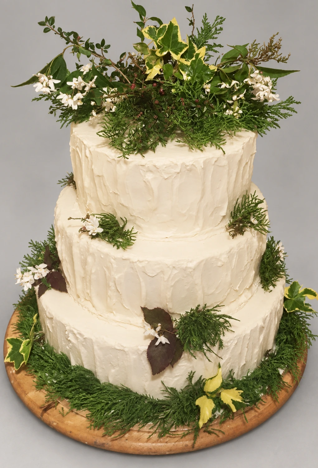 Three-tier textured ivory cake with fresh wildflowers, ferns and greenery on a wooden board