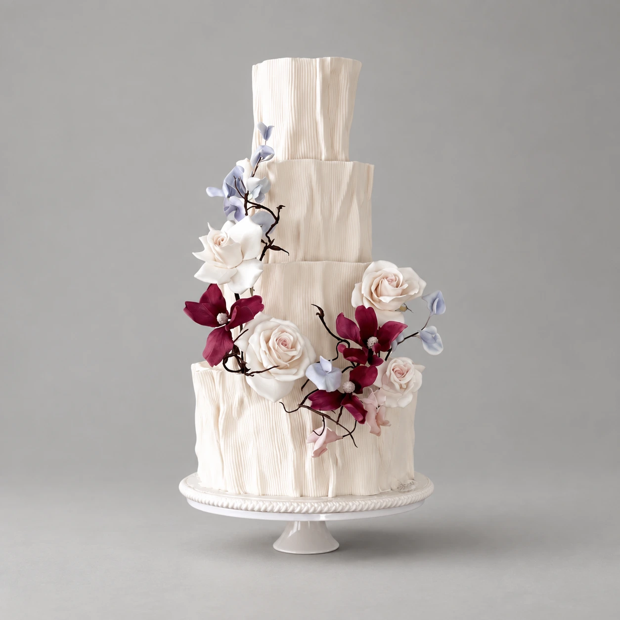 Four-tier ivory pleated cake with blush roses, burgundy blossoms and pale blue leaves