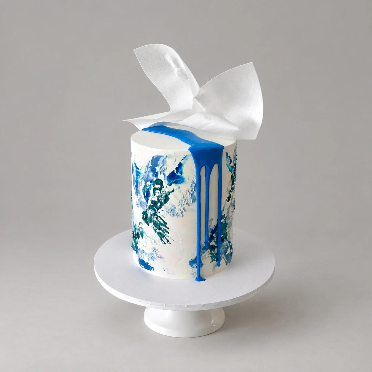 Single-tier ivory and blue textured cake with blue drip and a white sculptural sail