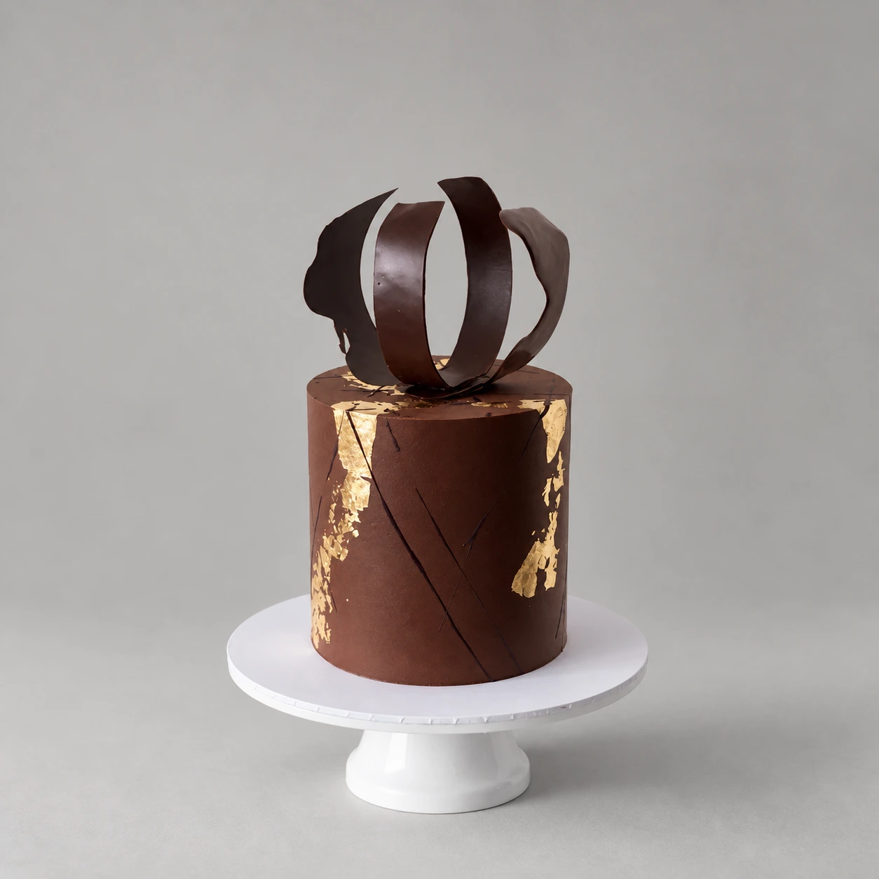 Single-tier chocolate cake with gold leaf and curled chocolate ribbons