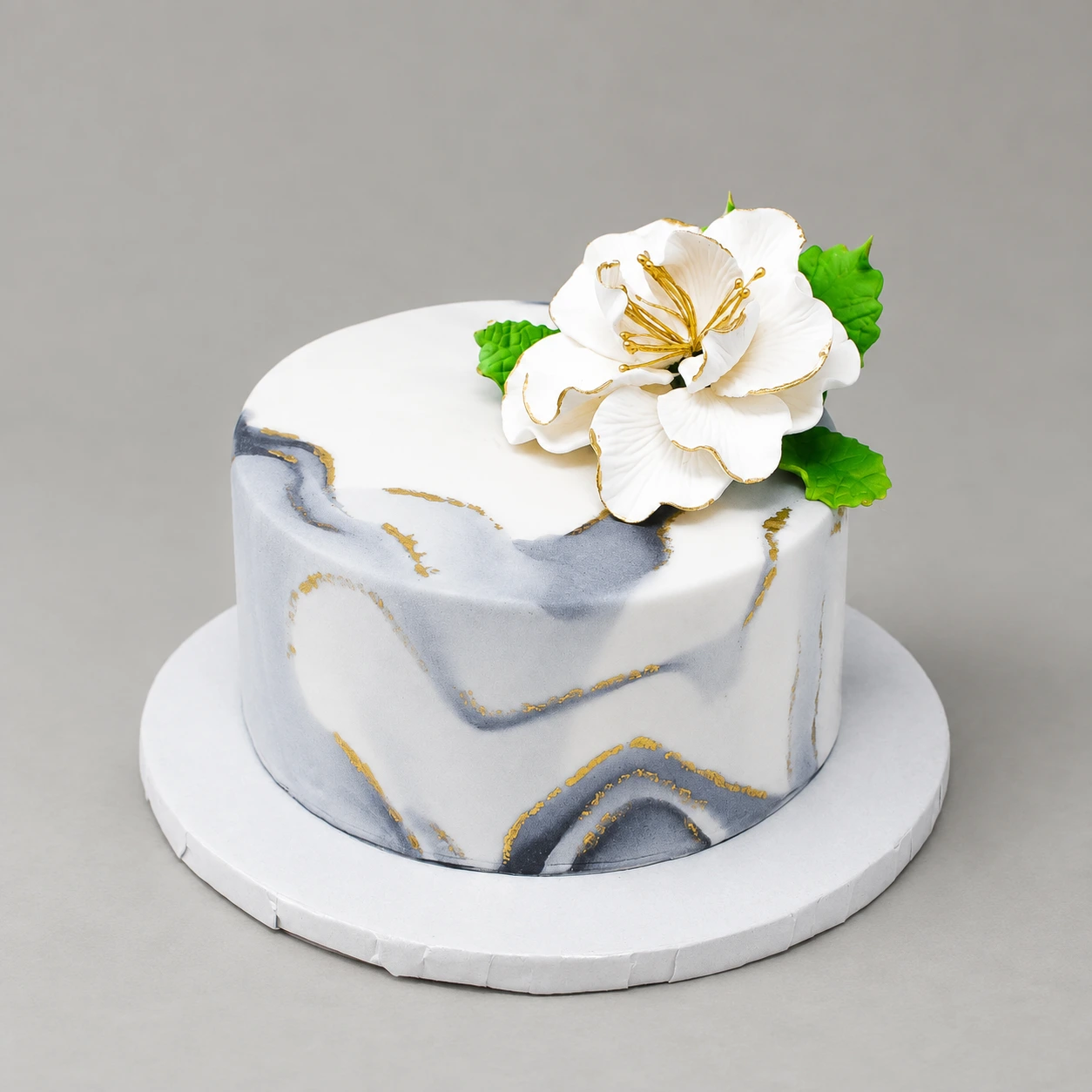 Single-tier grey and white marble cake with gold veins and a white gold-edged sugar flower