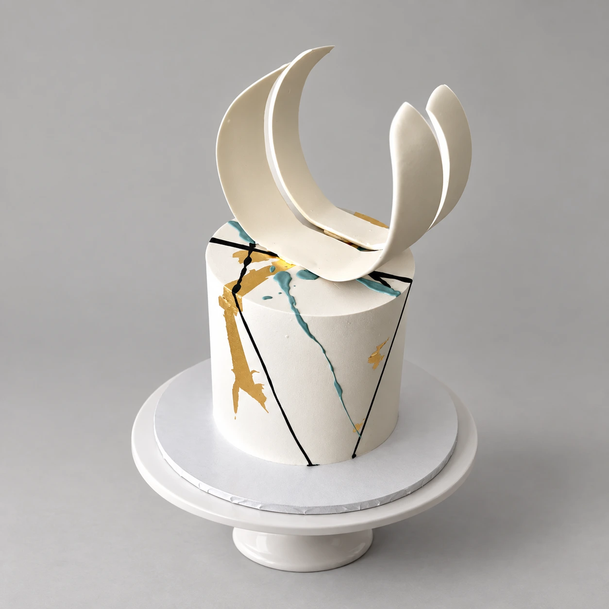 Single-tier ivory cake with black and teal abstract lines, gold leaf and white sculptural ribbons