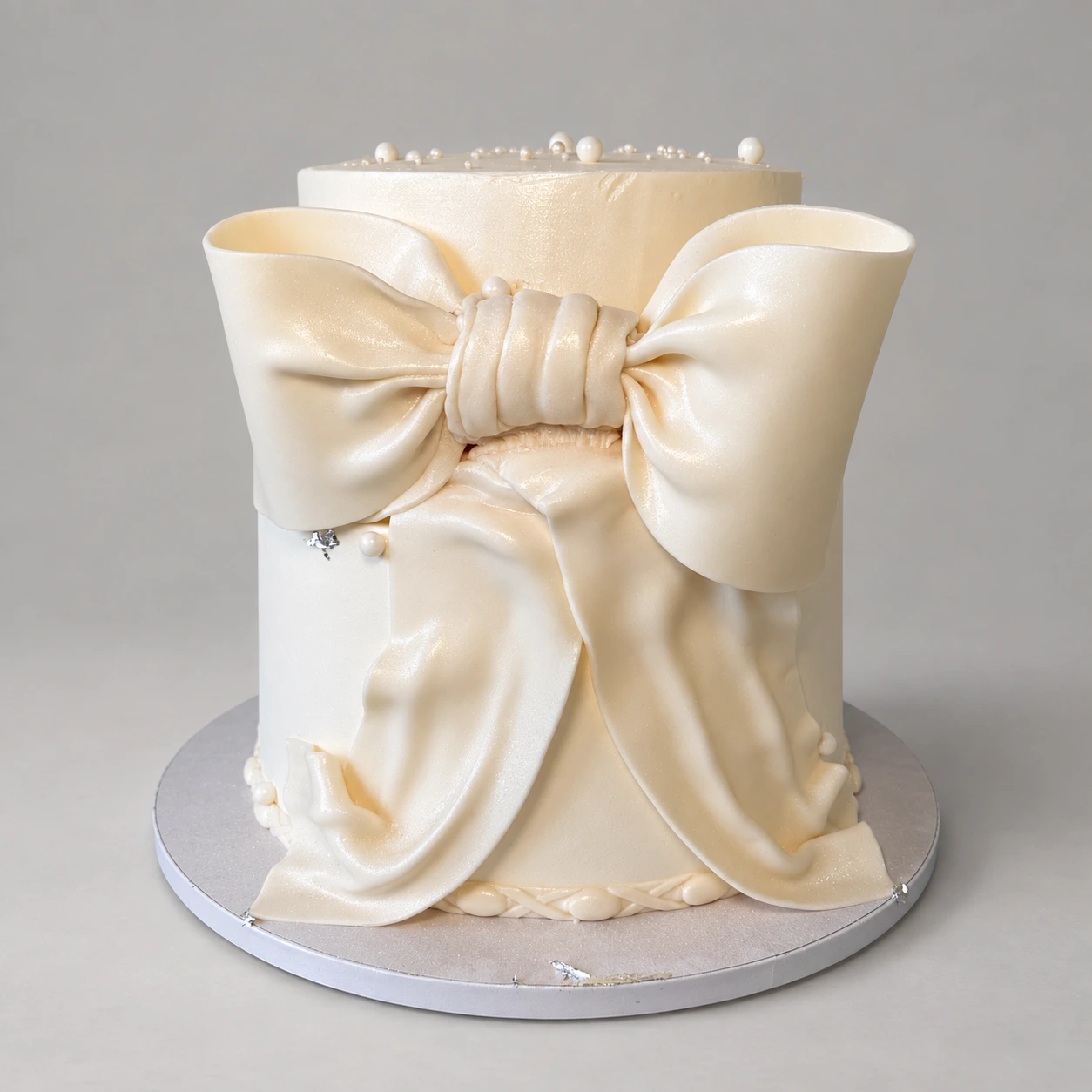 Single-tier ivory cake with a large pearlescent bow, draped tails and pearls