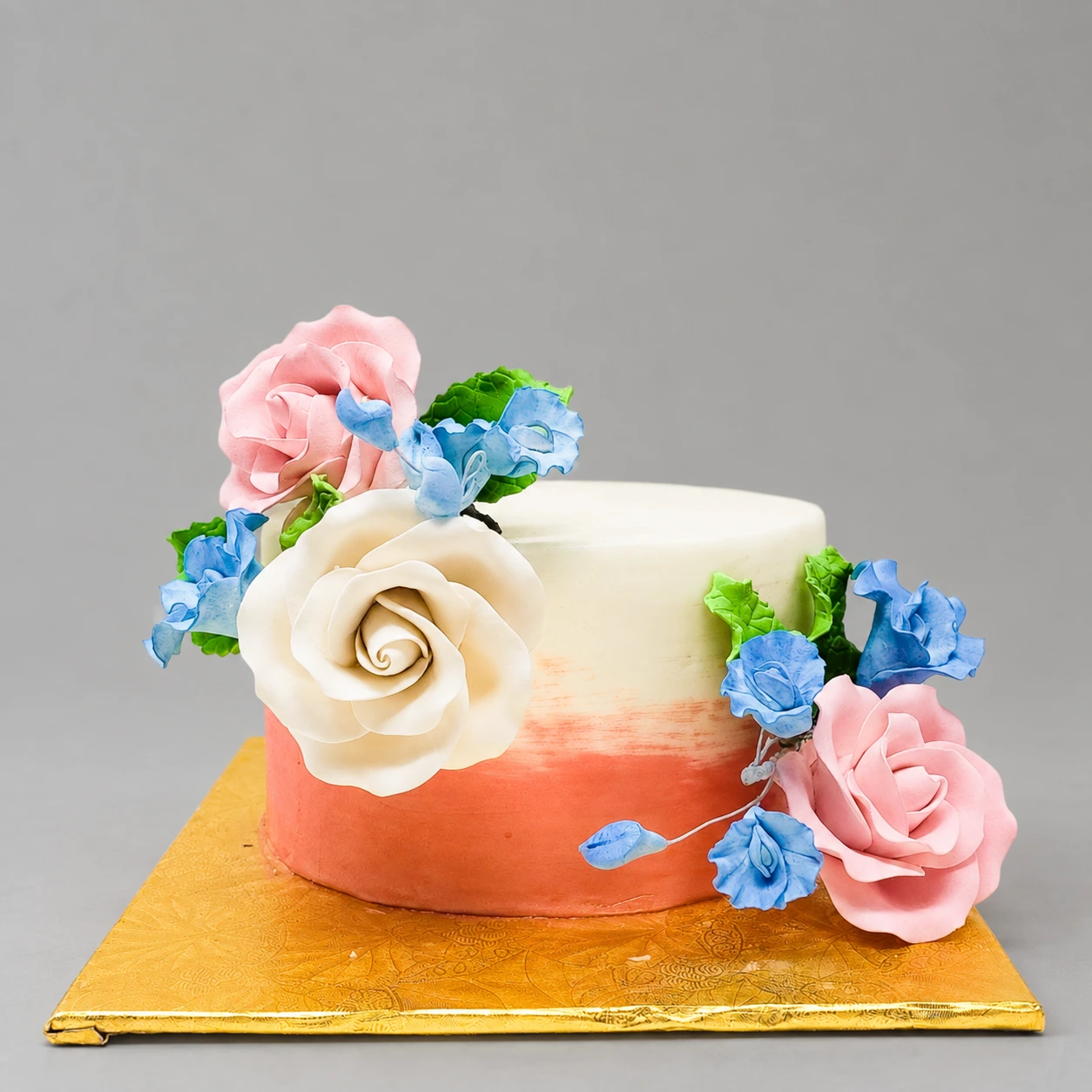 Single-tier ivory and rose gold cake with pink and ivory sugar roses, blue blossoms and green leaves