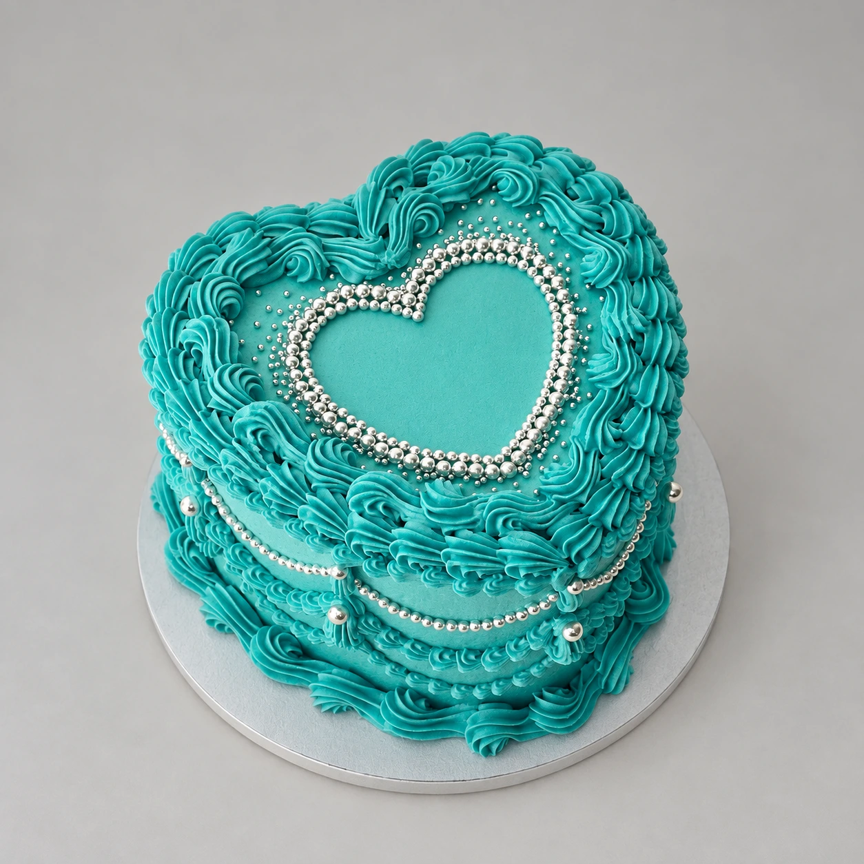 Single-tier turquoise heart cake with ornate piping and silver pearl swags